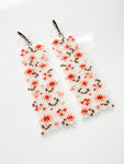 A pair of handmade earrings with translucent glass seed beads with an abstract floral patten.