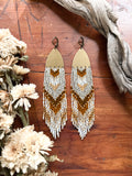 Long duster desert color unique beaded earrings on a brown wooden background.