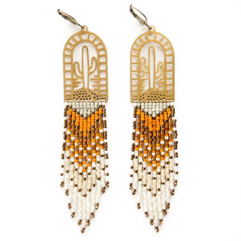 A pair of beaded earrings with browns and creams woven onto a brass cactus charm, photographed on a white background.