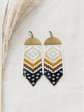 Handmade beaded fringe earrings by Certain Notions Designs crafted with Miyuki Delica seed beads in neutral browns on a raw-brass charm photographed on beige linen.